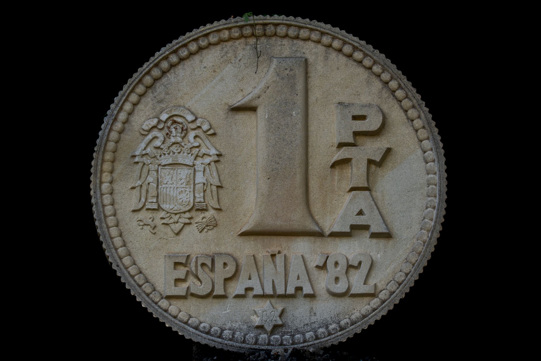 Large stone sculpture of a 1 peseta coin from Spain, 1982, with detailed engravings.
